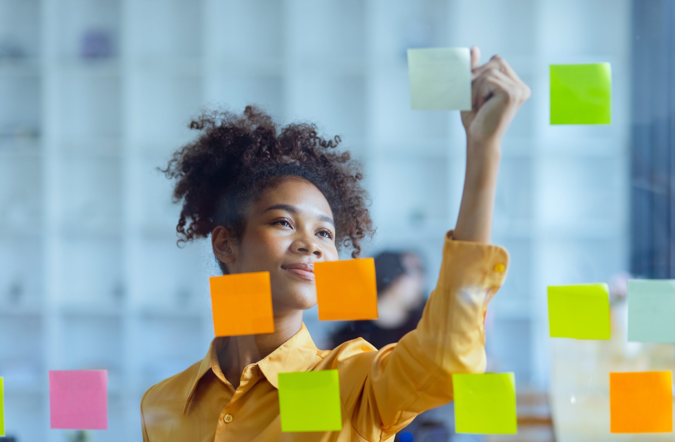 Young African American stylish woman working on project plan using sticky papers notes on glass wall, people meeting to share idea, Business design planning concepts.
