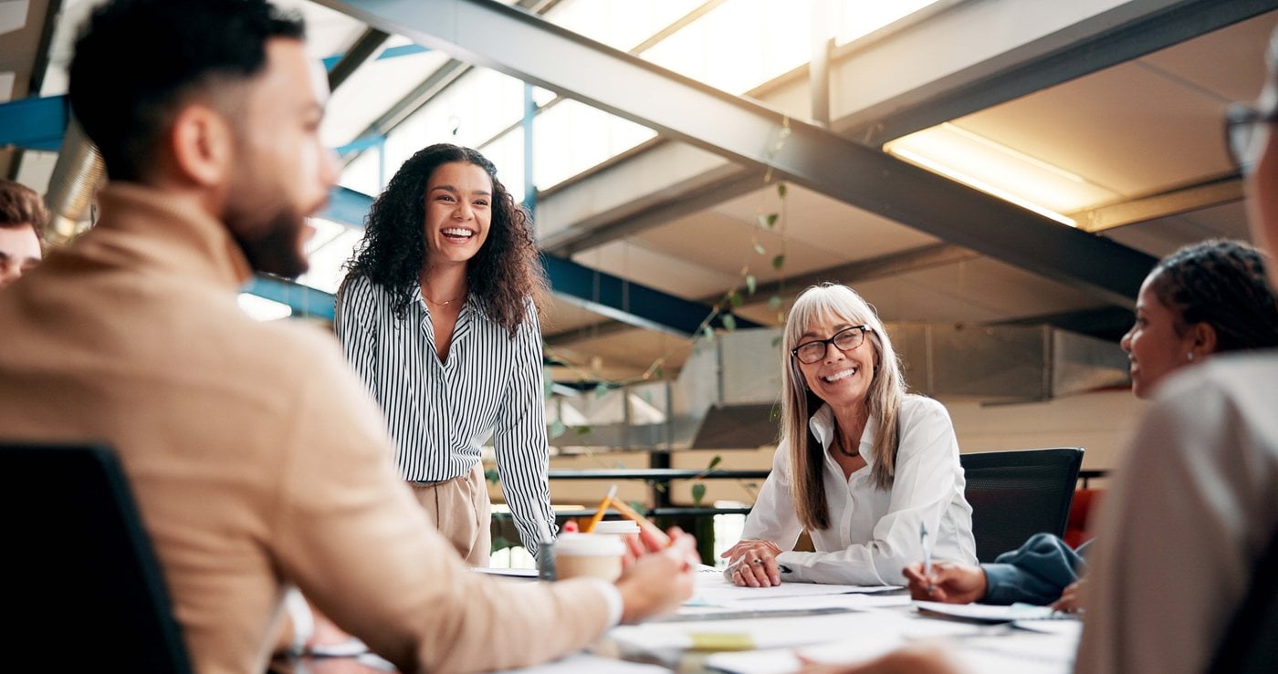 Colleagues laughing together around a conference table in a bright office