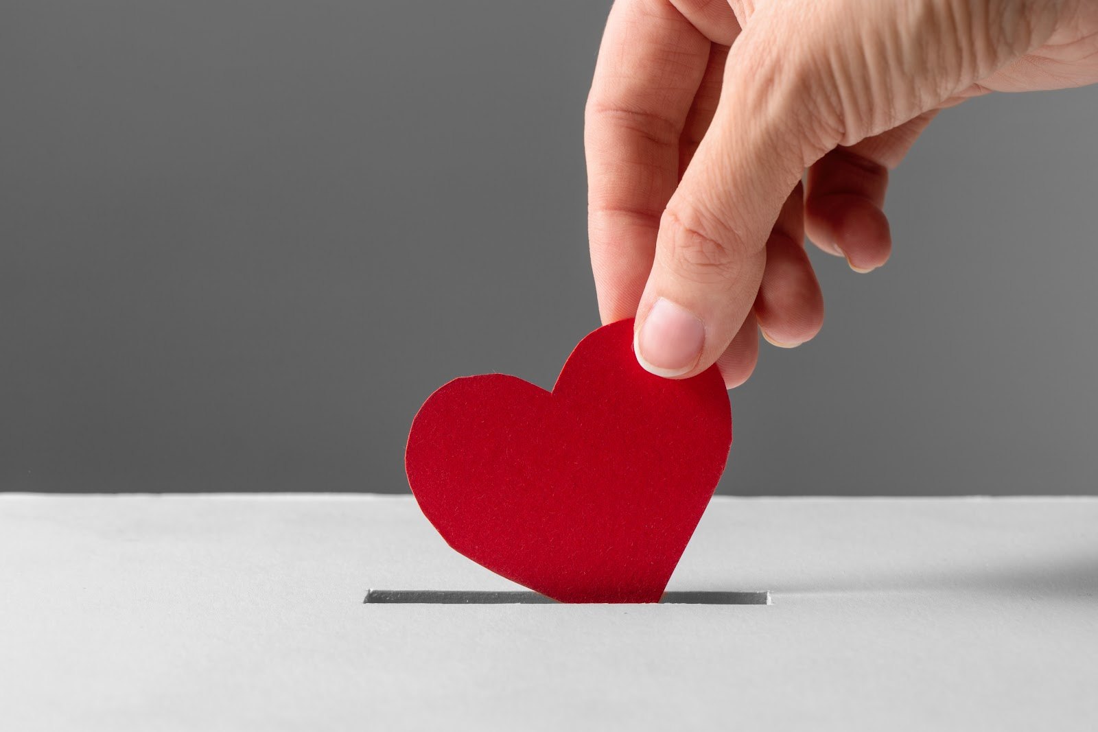 A hand placing a red paper heart into a donation box