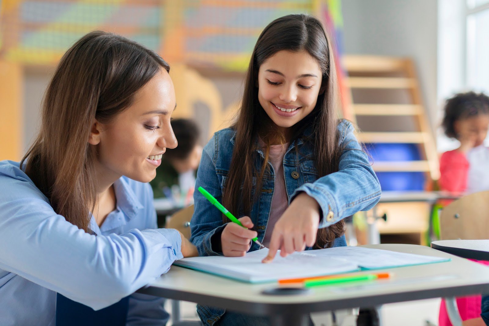 A teacher helping a smiling student with her work in a classroom