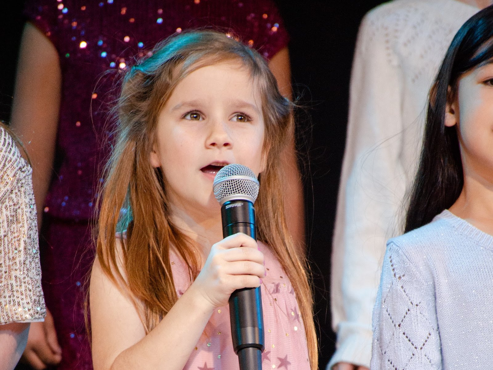 A young chorus member singing a solo into a microphone on stage