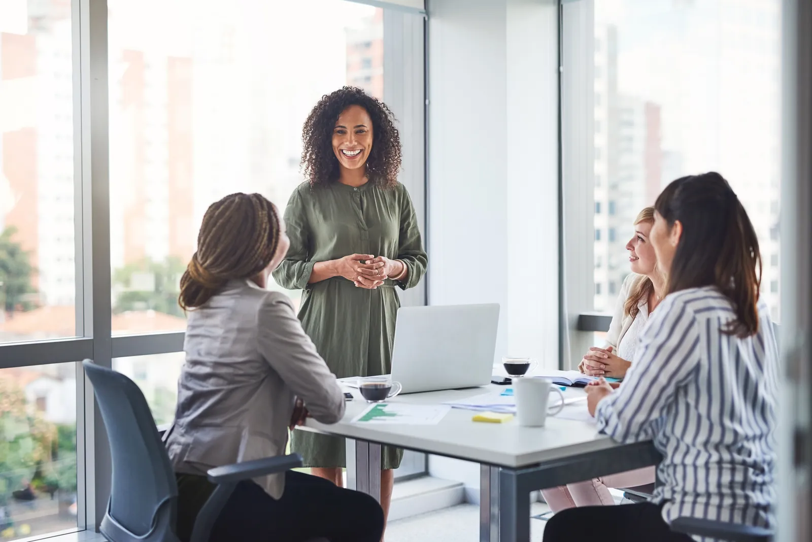A smiling woman stands and leads a conversation with three colleagues at a conference table