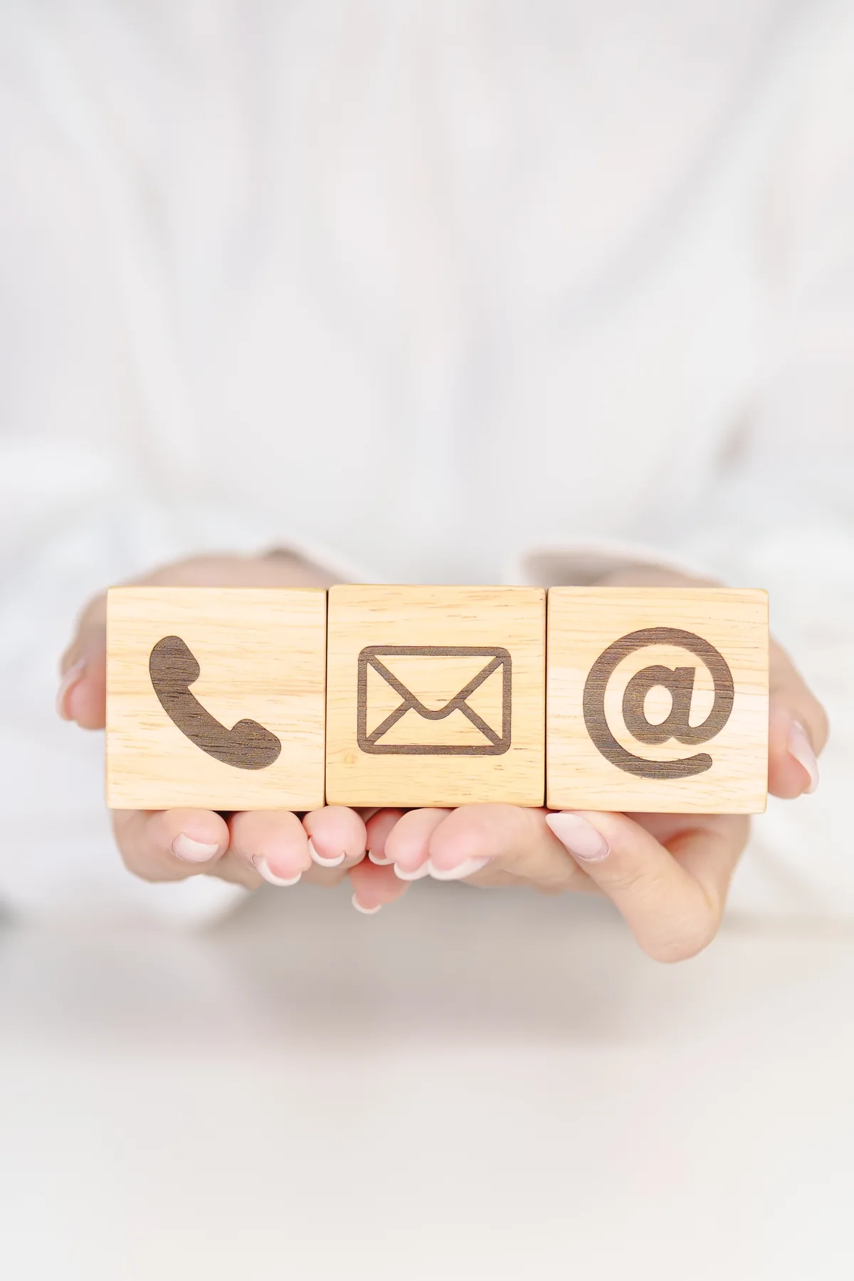 Hands hold three wooden blocks marked with phone, mail and email symbols