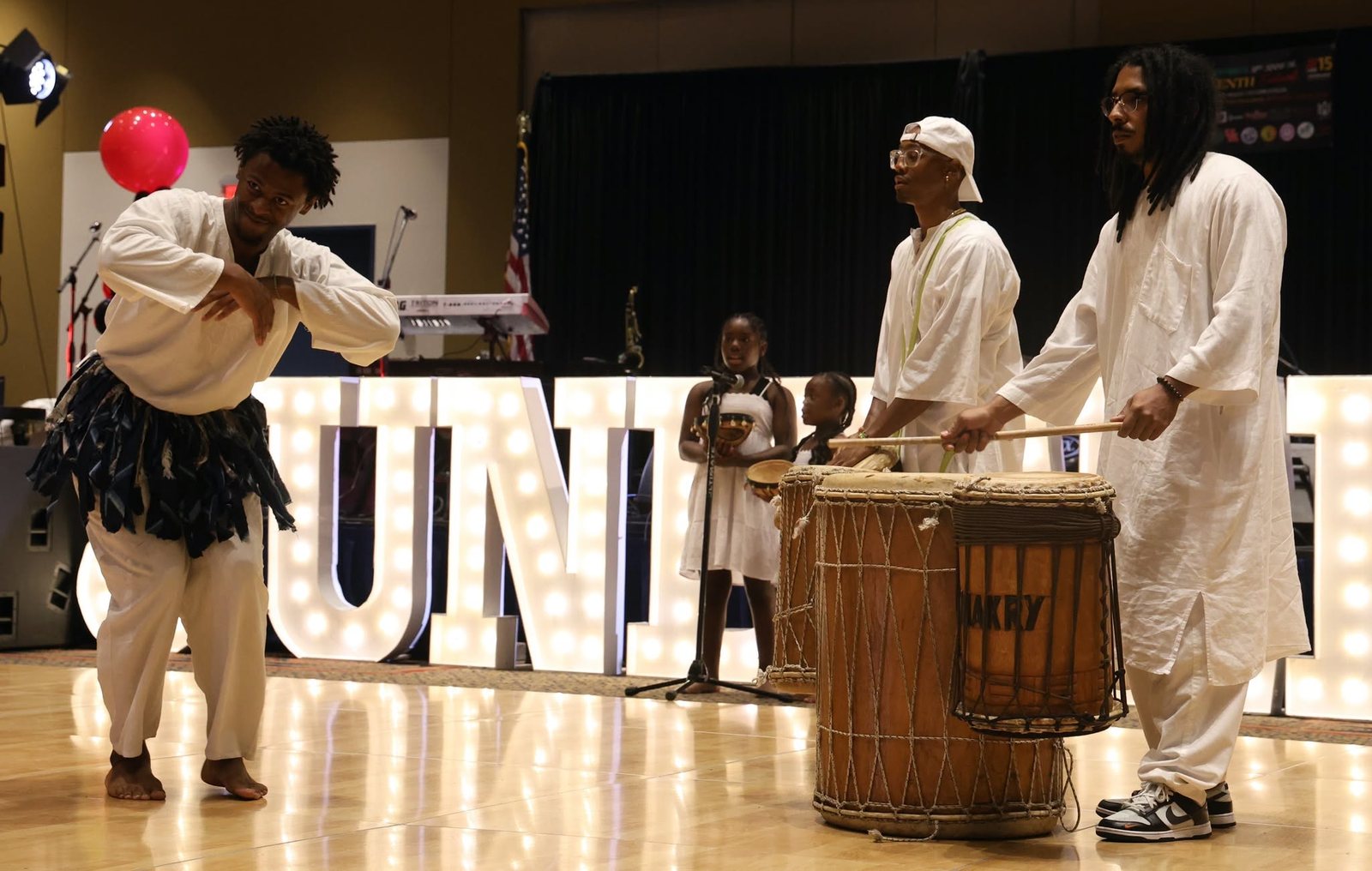 Drummers and a dancer perform in front of a lit-up Juneteenth sign